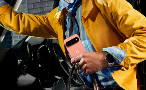 A person wearing a bright yellow jacket steps out of a car while holding a pink Google Pixel phone.